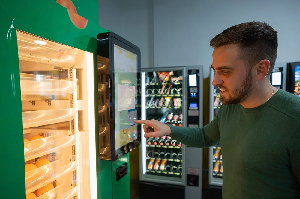 Man selecting fresh meal from green vending machine with spiral trays in vending area.