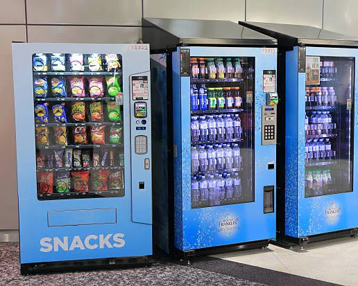 Row of blue vending machines including a snack machine and beverage vending machines lined up indoors.