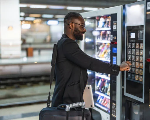 Business traveller using vending machine at transportation station, pressing keypad to select snack.