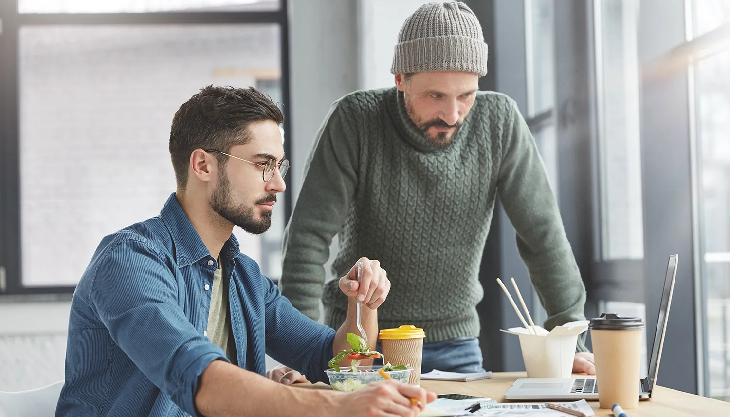 Two male coworkers in an Atlanta office enjoying fresh salad lunches and coffee together at their desks during a break, illustrating the convenience of Vendgo micro market meals.