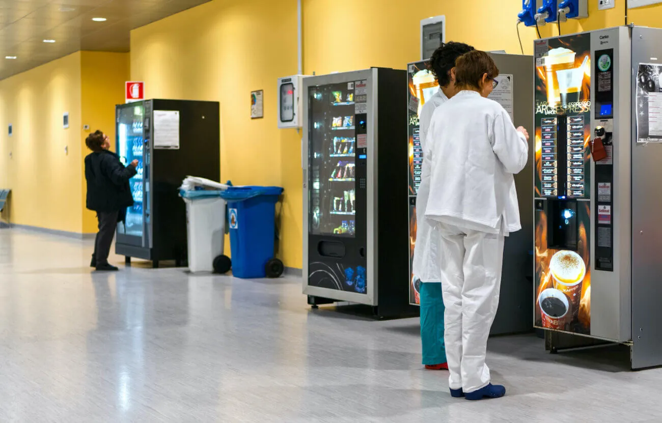 Hospital staff in scrubs using vending machines in a hospital hallway.