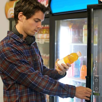 Young employee in an Atlanta warehouse selects a cold drink from a Vendgo smart cooler, illustrating convenient access to beverages through micro market vending.