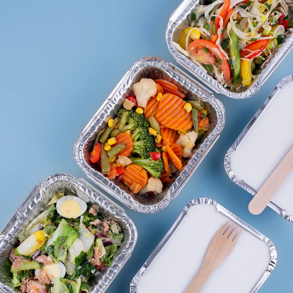 Healthy meal prep containers with fresh vegetables, salads and a wooden fork on a blue background.