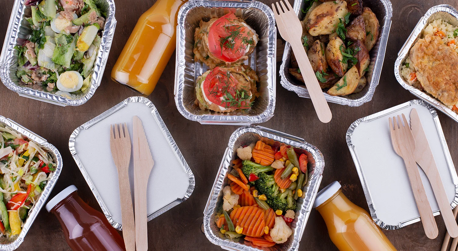 Assorted healthy meals in aluminum containers accompanied by juice bottles and wooden cutlery, representing Vendgo's fresh meal offerings for micro markets in Atlanta schools.