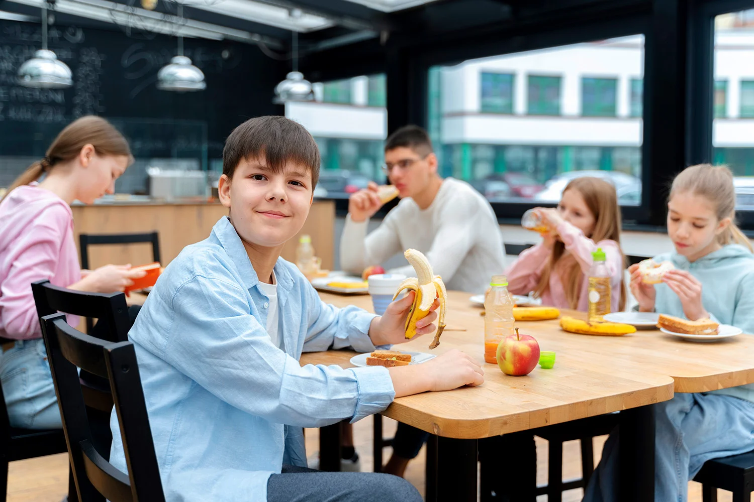 Group of schoolchildren sitting at a cafeteria table eating bananas and sandwiches during lunch, representing healthy snack options provided by Vendgo's micro market vending in Atlanta schools.