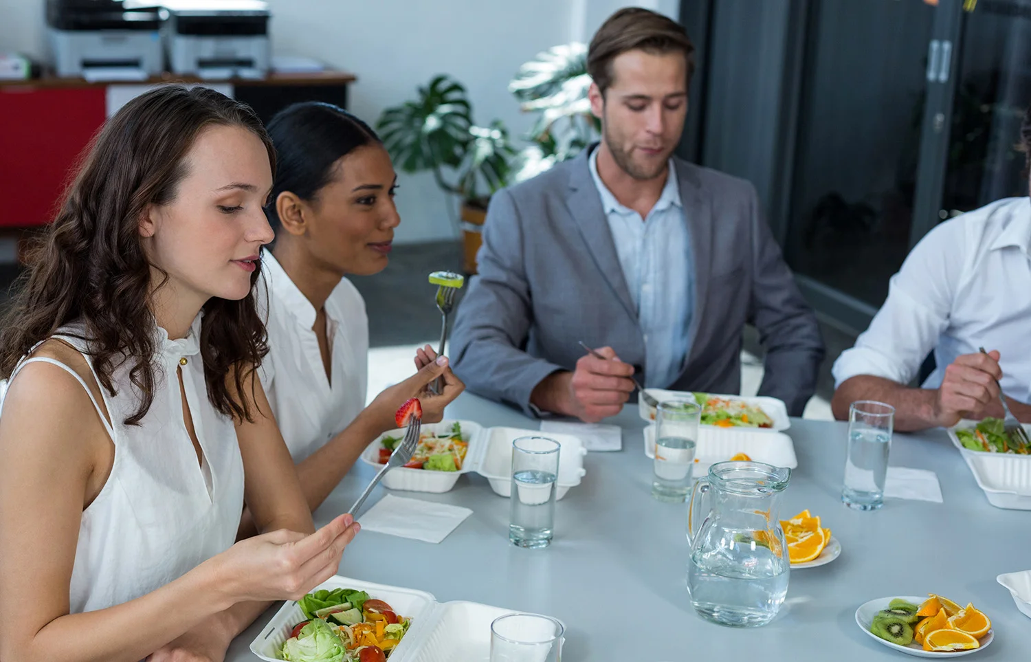 Business executives at an Atlanta office sit around a table enjoying healthy lunches and conversation, highlighting the benefits of Vendgo micro market meals.